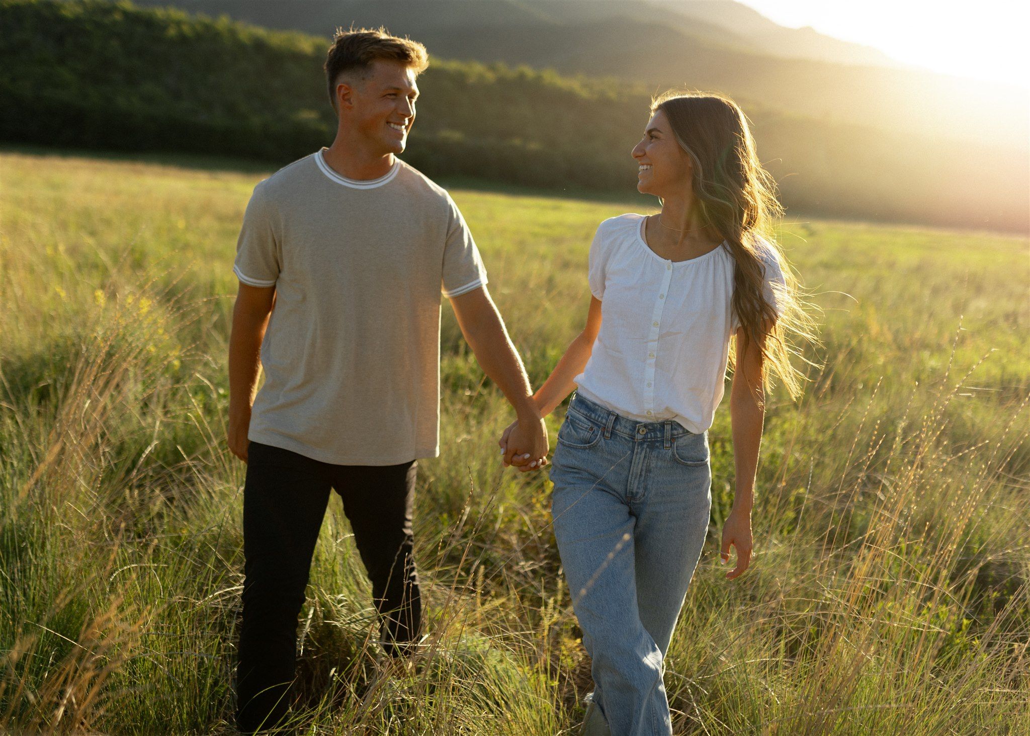 Romantic couple walking through a golden field at sunset.