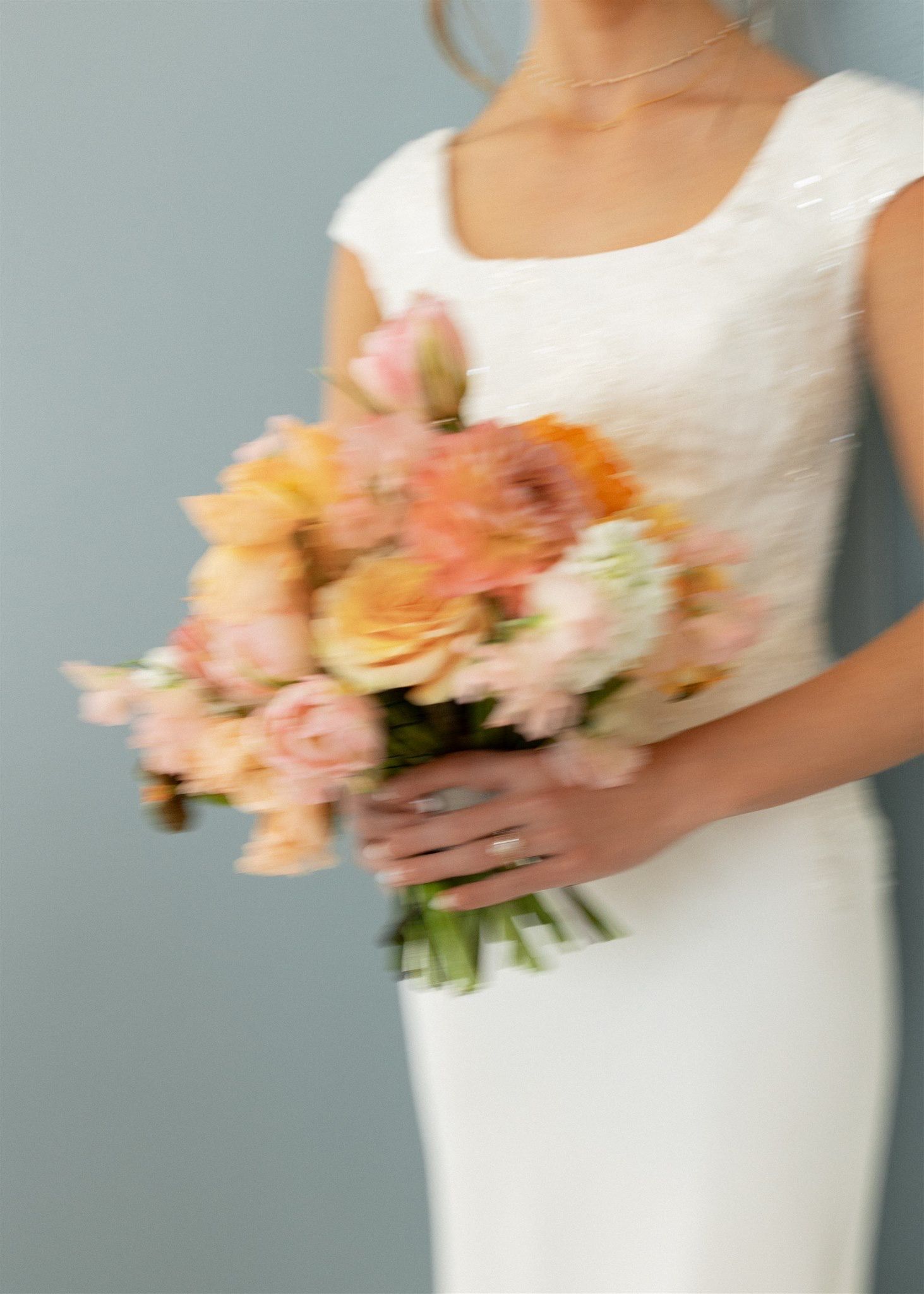 A bride in a white gown holding a lush bouquet of peach, pink, and orange roses and flowers.
