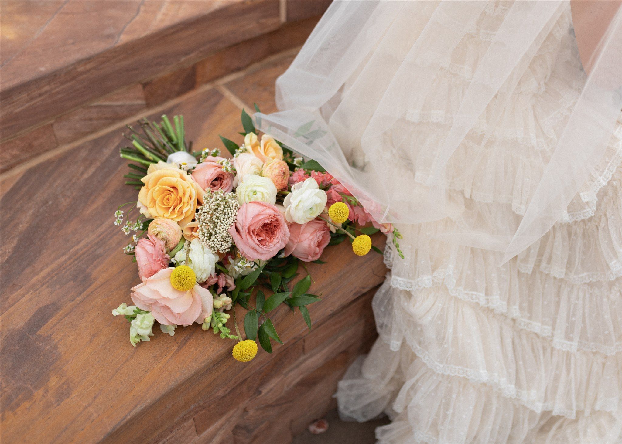 Delicate arrangement of peach and pink roses with white wedding dress details.