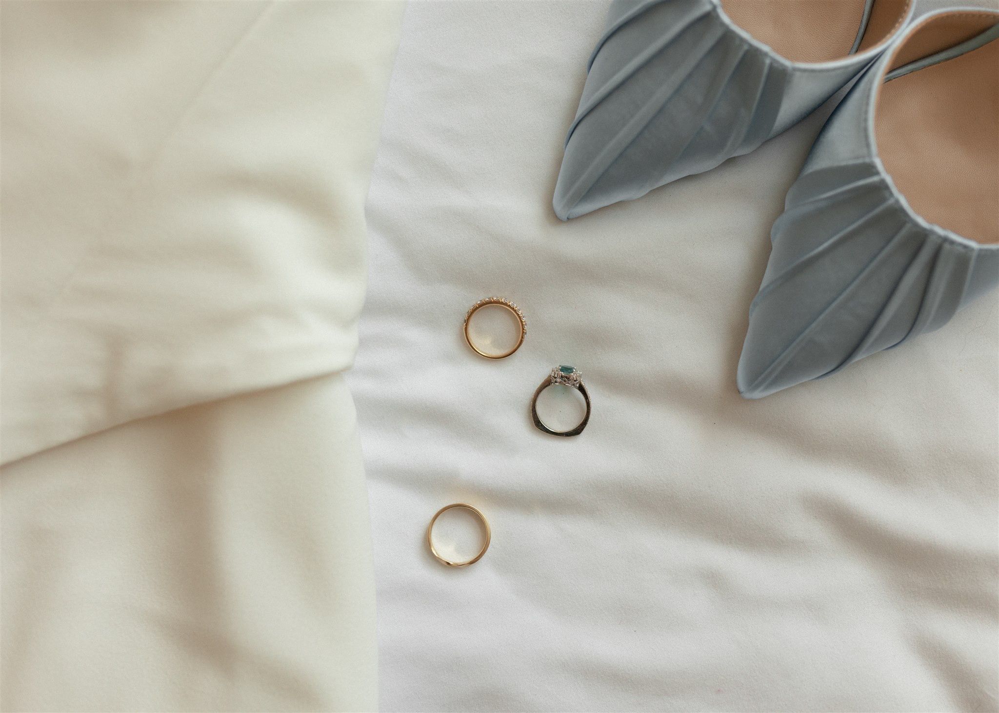 Three gold wedding rings and engagement ring laid flat near blue pointed-toe heels.