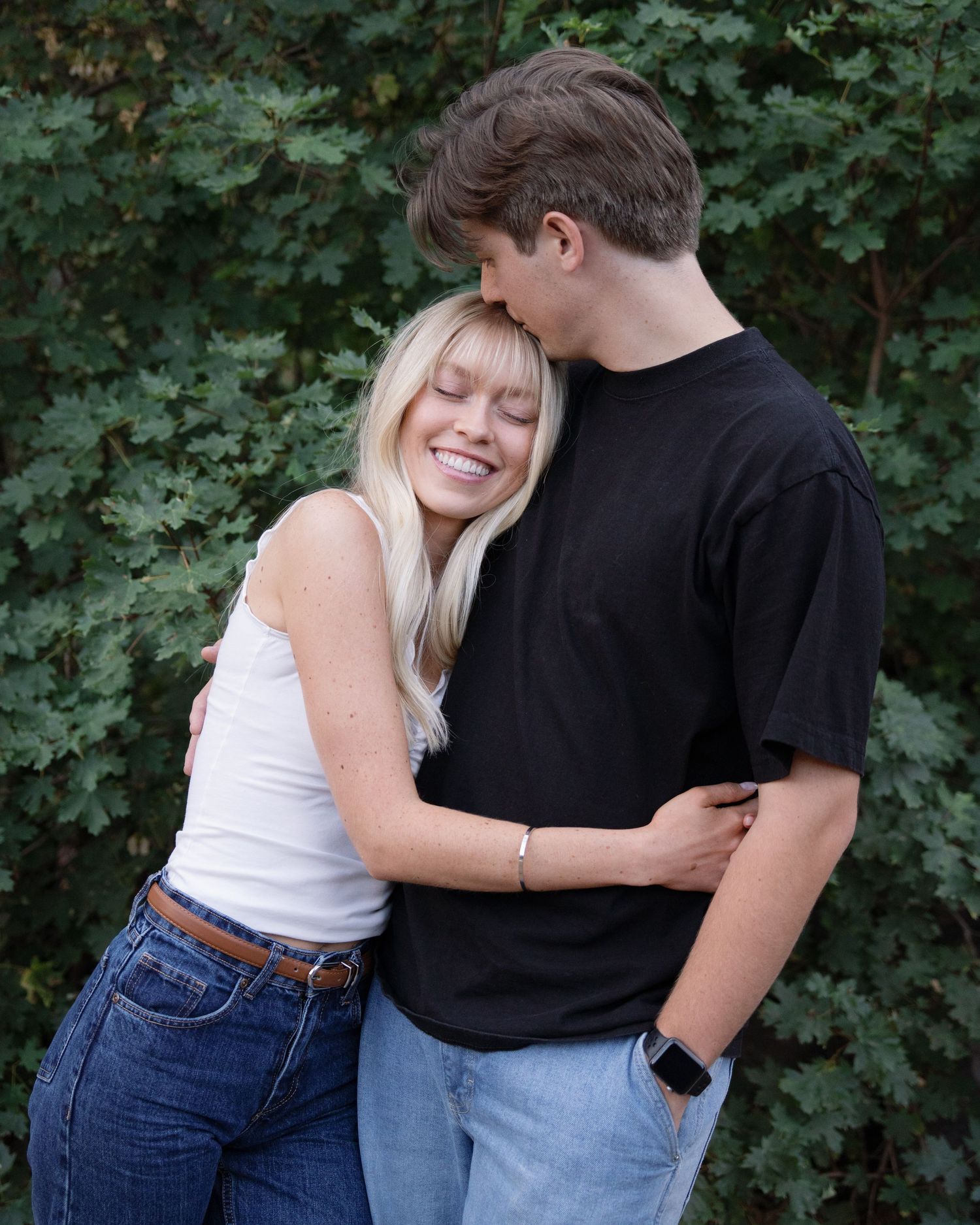 Casual couple embracing against green leafy background.