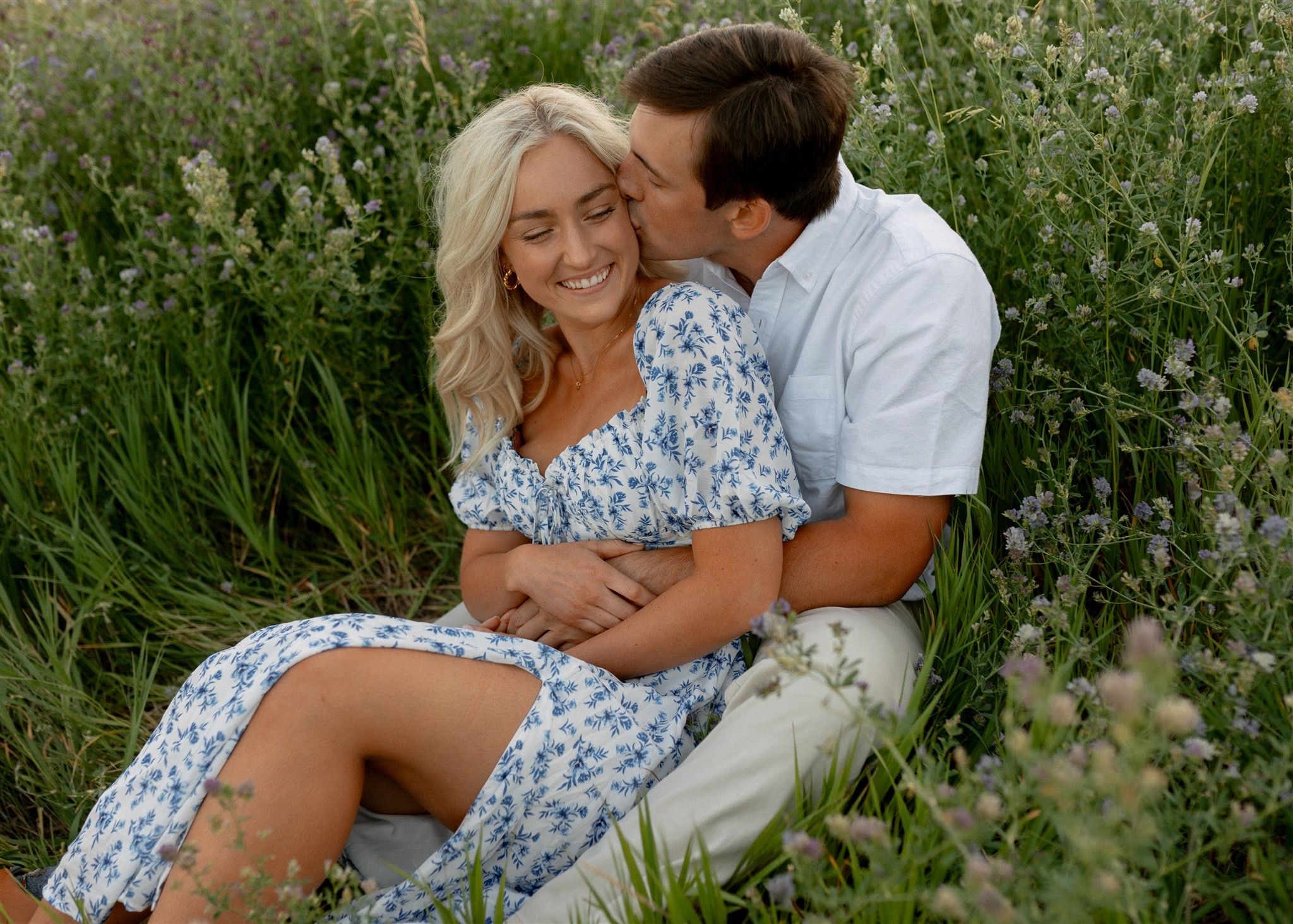 A smiling blonde woman in a floral dress sitting with her partner in a lavender field.